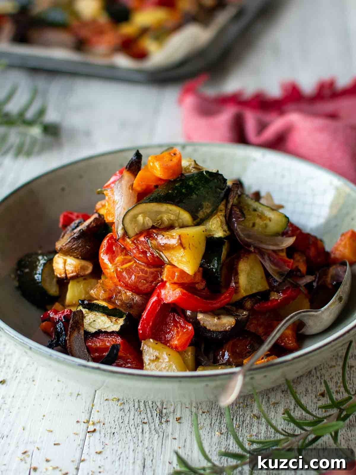 Italian Roasted Vegetables Recipe 2 Plate of Italian Roasted Vegetables piled high with a spoon inserted and a red napkin in the background.