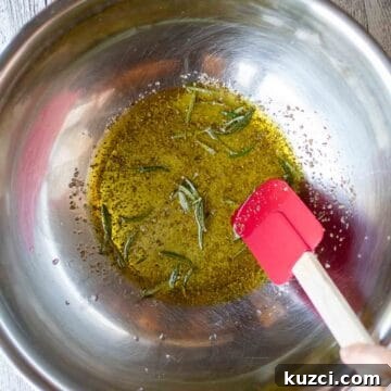 Italian Roasted Vegetables Recipe 5 Oil and herbs in a stainless steel bowl with a red spatula viewed from above.