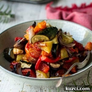 Italian Roasted Vegetables Recipe 10 Plate of Italian Roasted Vegetables piled high with a spoon inserted and a red napkin in the background.