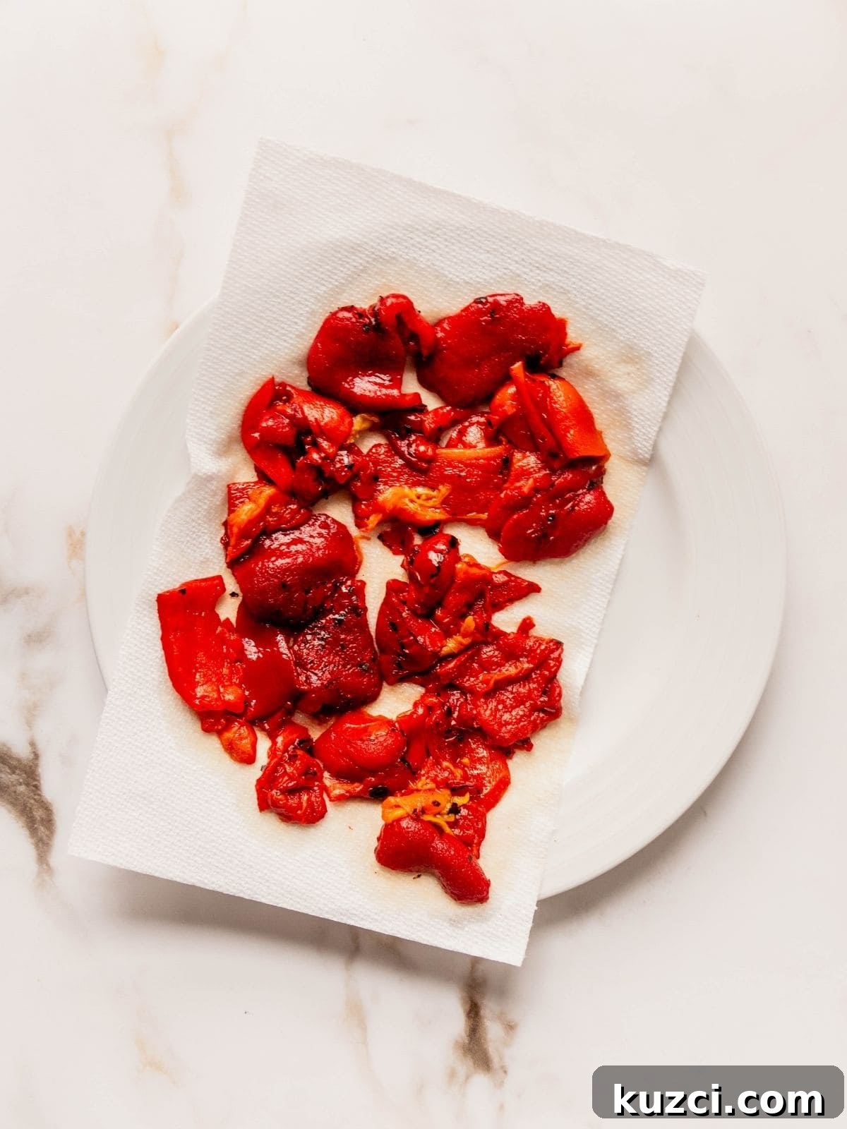 Roasted red pepper slices draining on a piece of paper towel on a plate.