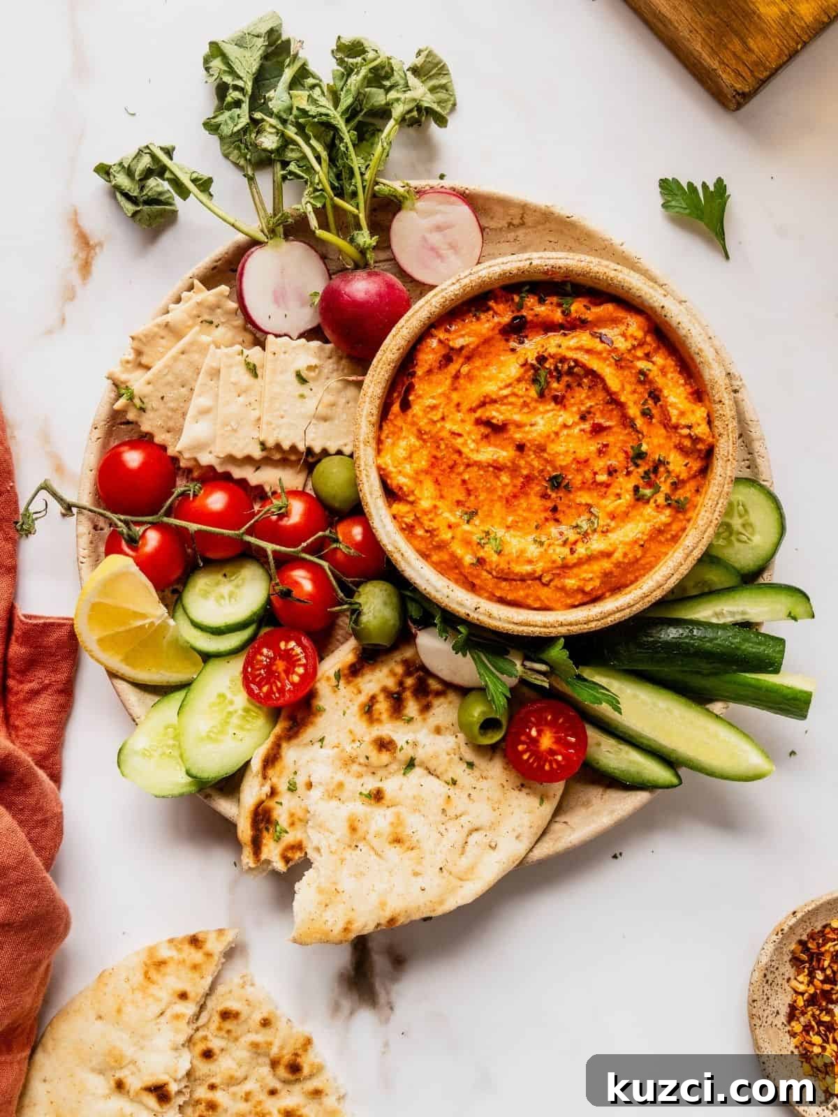 Bowl of red pepper feta dip (also known as Tirokafteri or Htipiti) on a plate garnished with parsley and served with bread, vegetables and olives.
