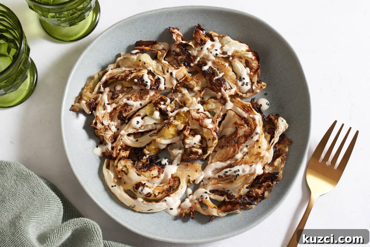 Charred Sheet Pan Cabbage with Tahini Sauce 2 Charred cabbage topped with tahini sauce and black sesame seeds on a gray plate, a gold fork is on the right, green glasses are in the upper left.