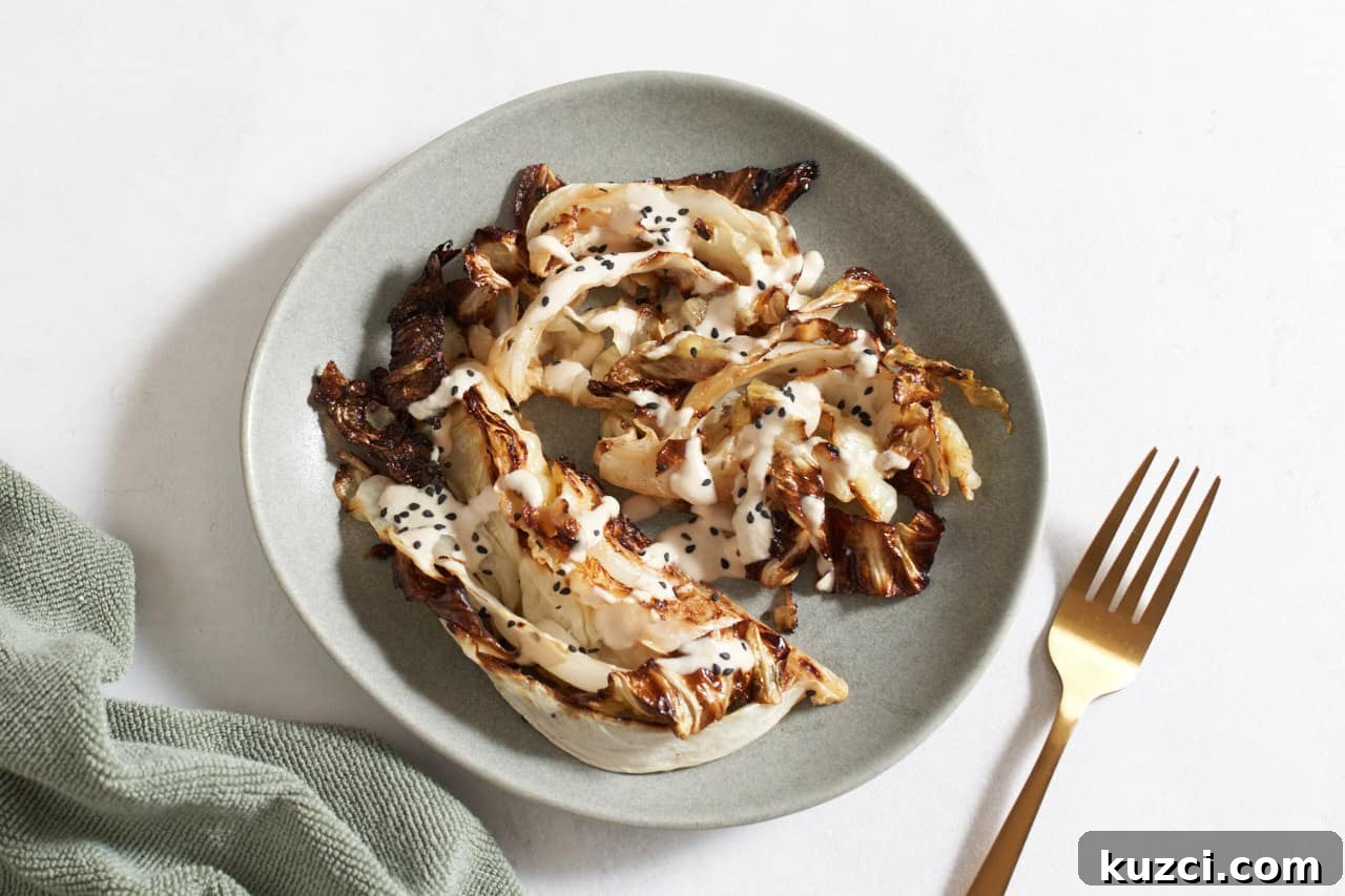 Charred Sheet Pan Cabbage with Tahini Sauce 7 Charred cabbage topped with tahini sauce and sesame seeds on a gray plate, a gold fork is on the right.