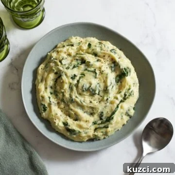 Colcannon potatoes on a gray plate. A spoon is on the right, two green glasses and a green towel are on the left.