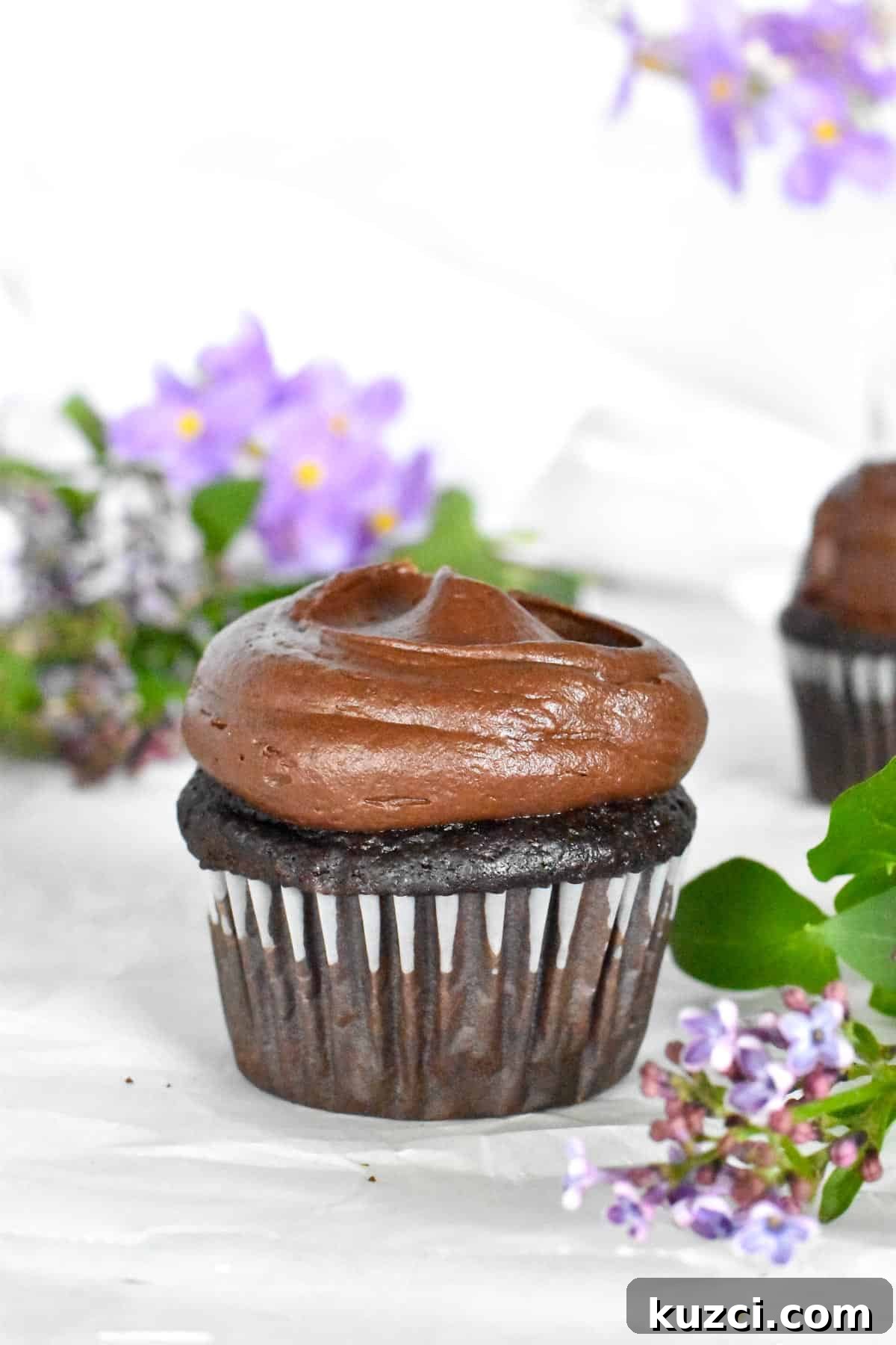 chocolate cupcake with purple flowers in background.