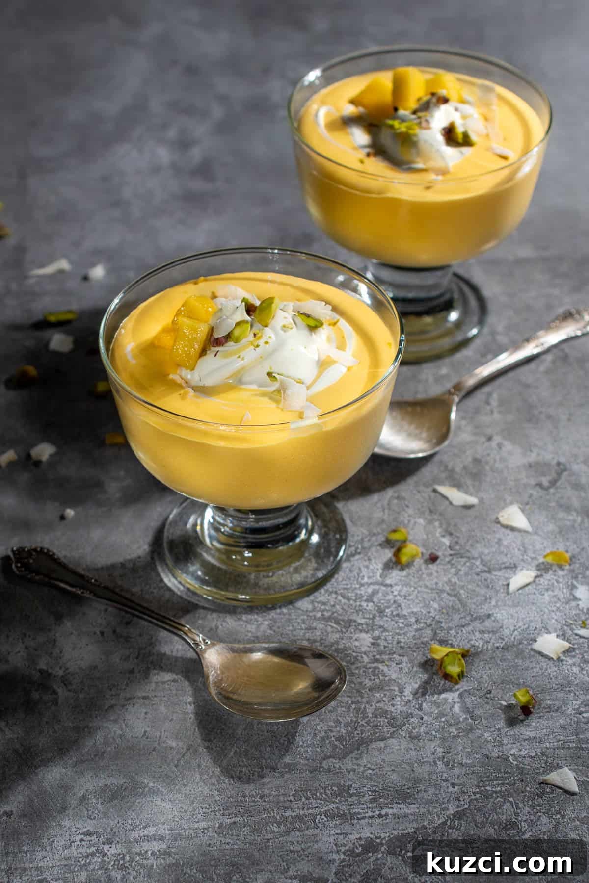 Creamy Mango Mousse Recipe 2 Two bowls of mango mousse in dessert cups with a swirl of cream and nuts.