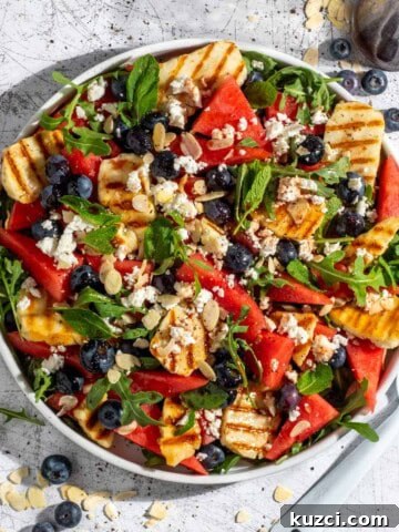 Grilled halloumi and watermelon salad on a large white salad plate with blueberries scattered on the surface around it.