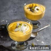 Creamy Mango Mousse Recipe 14 Two bowls of mango mousse in dessert cups with a swirl of cream and nuts.