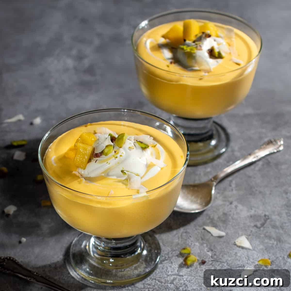 Creamy Mango Mousse Recipe 9 Two bowls of mango mousse in dessert cups with a swirl of cream and nuts.