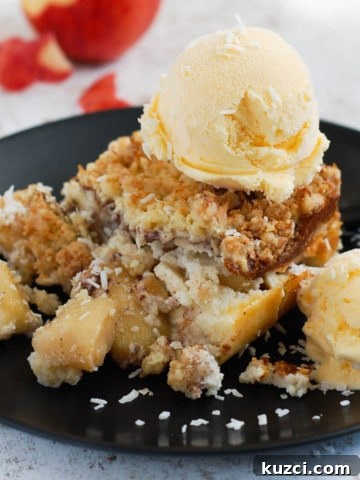 Apple crumble tart, topped with ice cream on a black plate