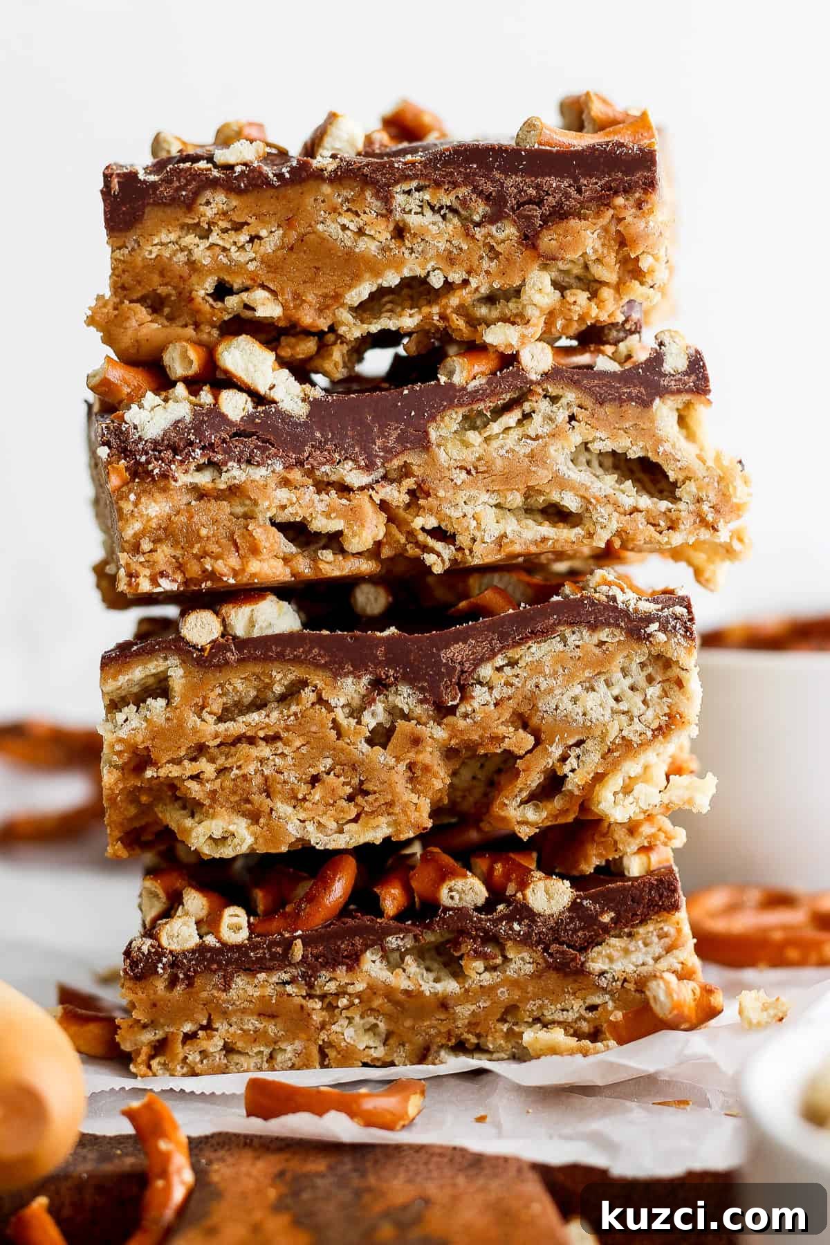 Peanut Butter Chex Bars Recipe 2 A stack of three layered peanut butter bars with a chocolate topping and crushed nuts on parchment paper.