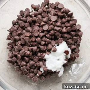 Peanut Butter Chex Bars Recipe 12 A bowl containing chocolate chips with a dollop of what appears to be white ingredient, possibly a dairy product such as cream or yogurt, on top, set against a neutral background.