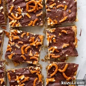 Peanut Butter Chex Bars Recipe 15 Chocolate-covered toffee bars topped with pretzel pieces on parchment paper, cut into rectangles, with a knife resting to the side.