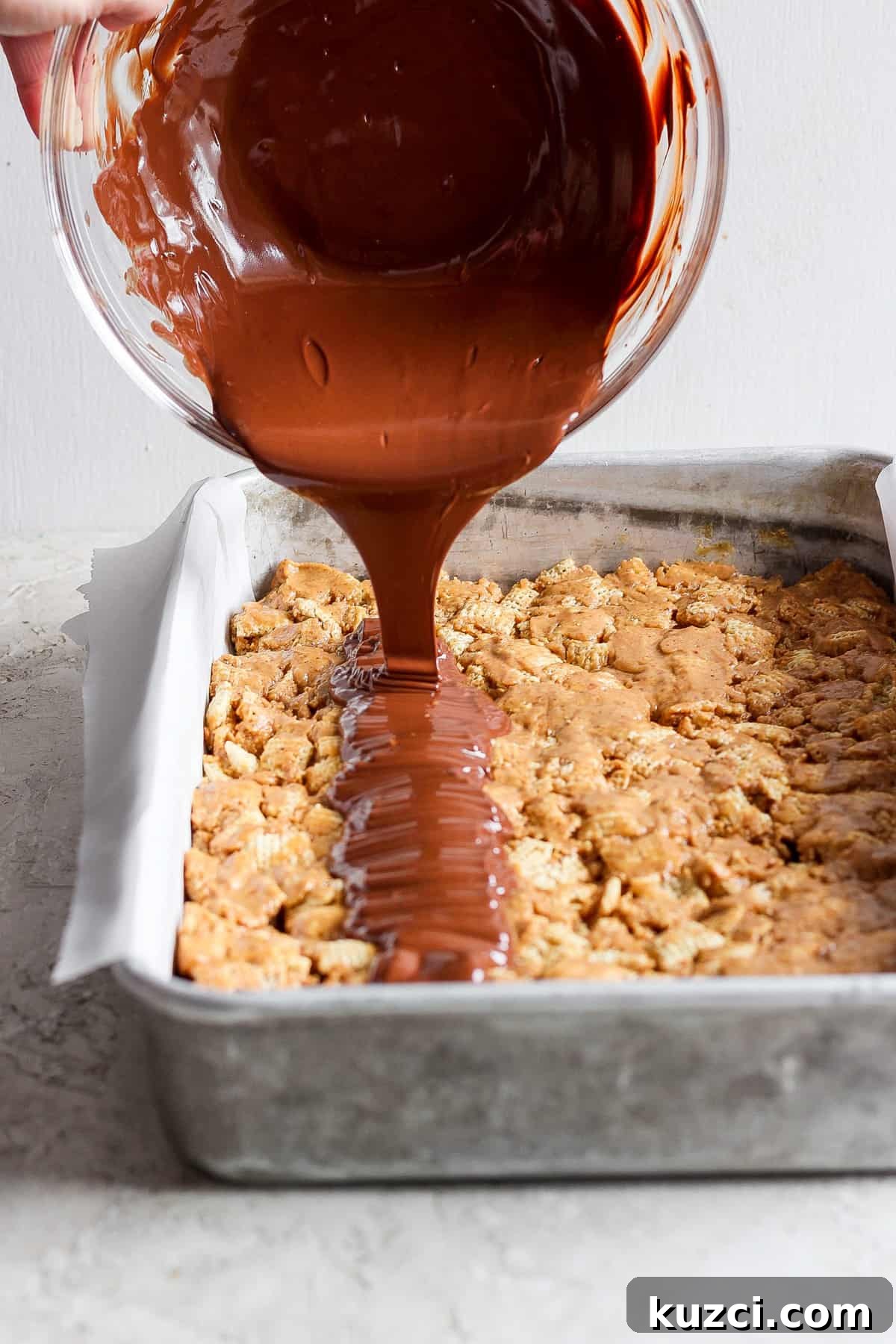 Peanut Butter Chex Bars Recipe 3 Chocolate sauce being poured onto a tray of baked dessert bars.
