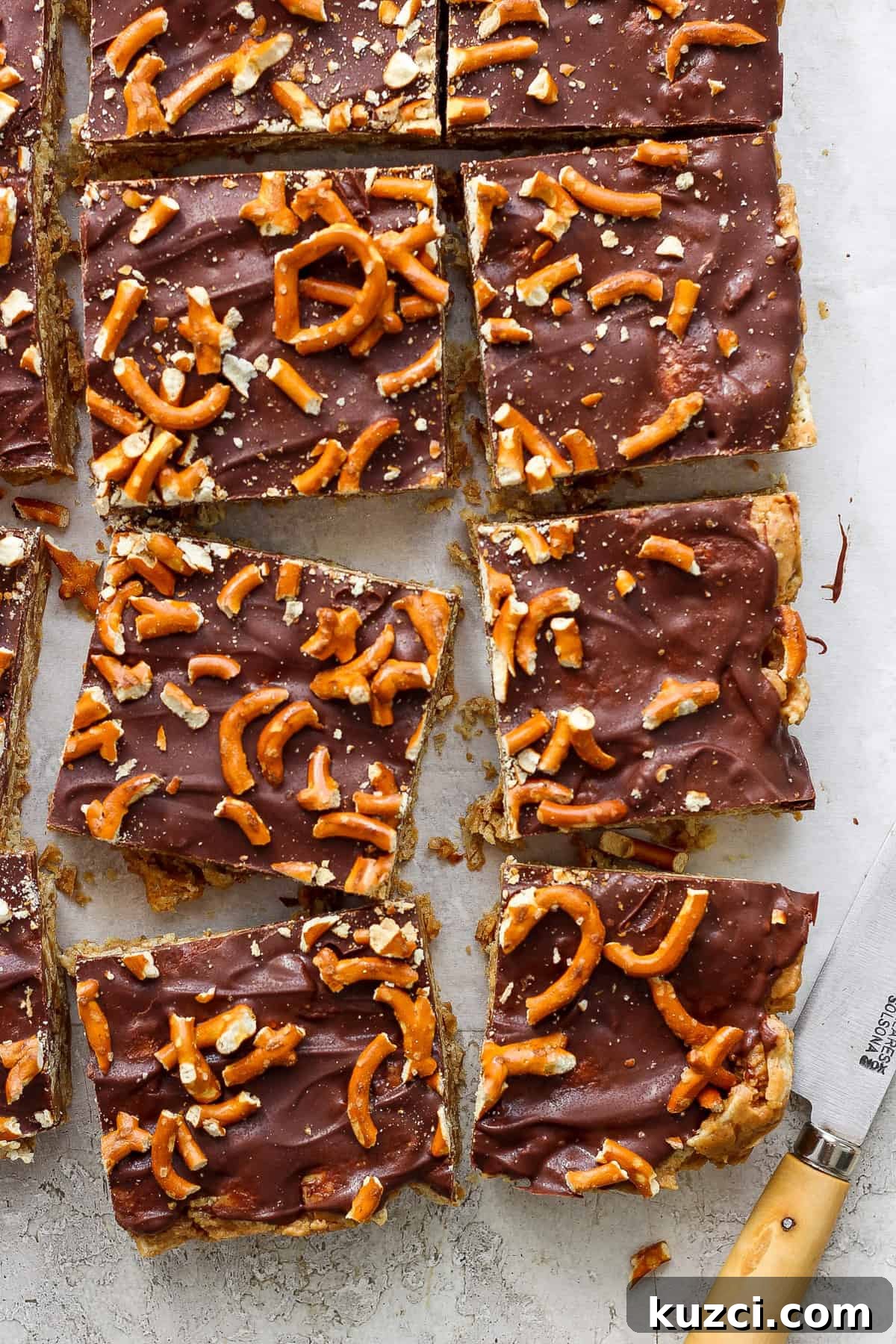 Peanut Butter Chex Bars Recipe 7 Chocolate-covered toffee bars topped with pretzel pieces on parchment paper, cut into rectangles, with a knife resting to the side.