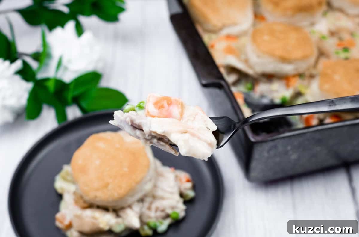 33 Fall Dinner Recipes Packed With Comfort Food Favorites 16 A fork holds a bite of chicken pot pie with vegetables and biscuit topping, with a plate and baking dish of the same meal in the background.