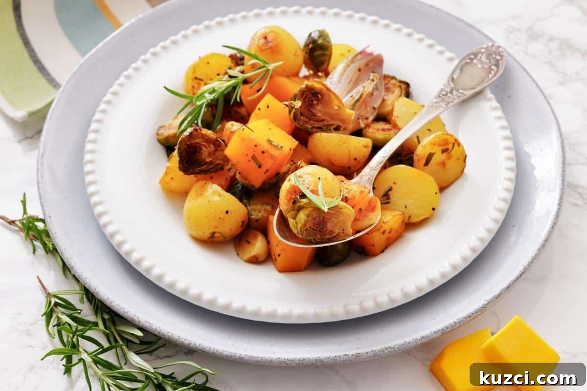 33 Fall Dinner Recipes Packed With Comfort Food Favorites 18 A plate of roasted vegetables including potatoes, Brussels sprouts, and squash, garnished with fresh herbs, with a serving spoon on a white plate.