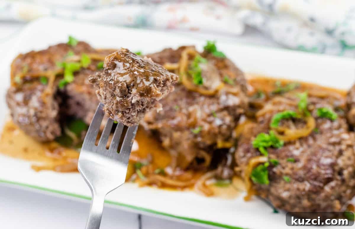 33 Fall Dinner Recipes Packed With Comfort Food Favorites 3 A close-up of a fork holding a piece of cooked Mississippi Salisbury steak with gravy and onions, with more steak pieces and sauce on a white plate in the background.
