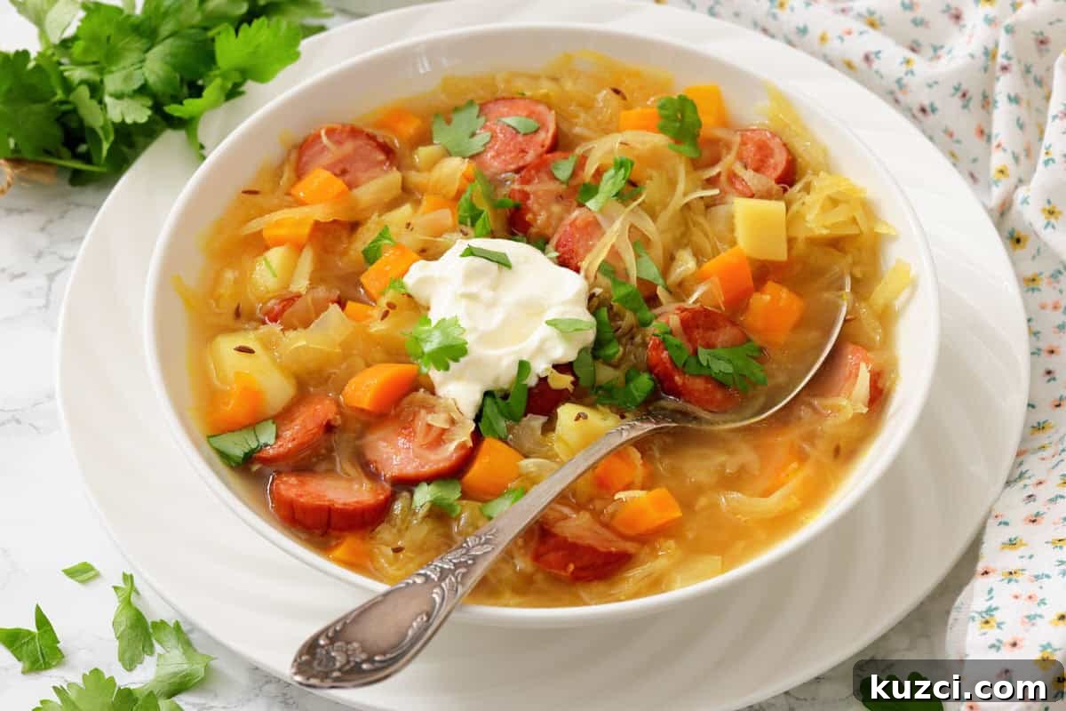 33 Fall Dinner Recipes Packed With Comfort Food Favorites 10 A bowl of soup with sliced sausage, potatoes, carrots, cabbage, garnished with fresh herbs and a dollop of sour cream, with a spoon resting in the bowl.