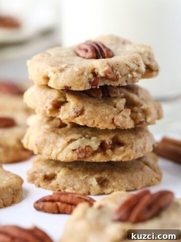 pecan sandies stacked on a white table with pecan halves scattered around.