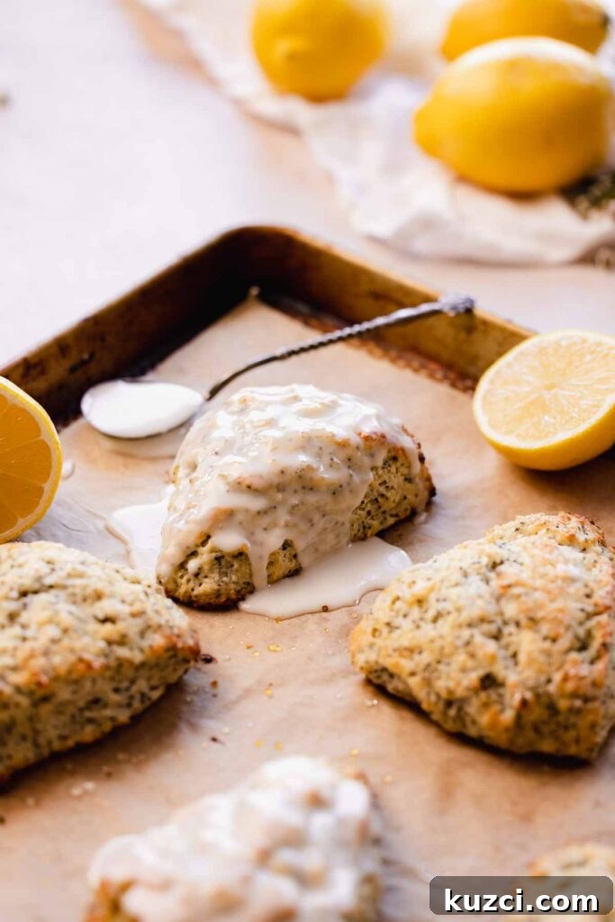 Lemon Poppy Seed Scones with Zesty Glaze 2 lemon poppy seed scones with lemon glaze on parchment lined baking sheet