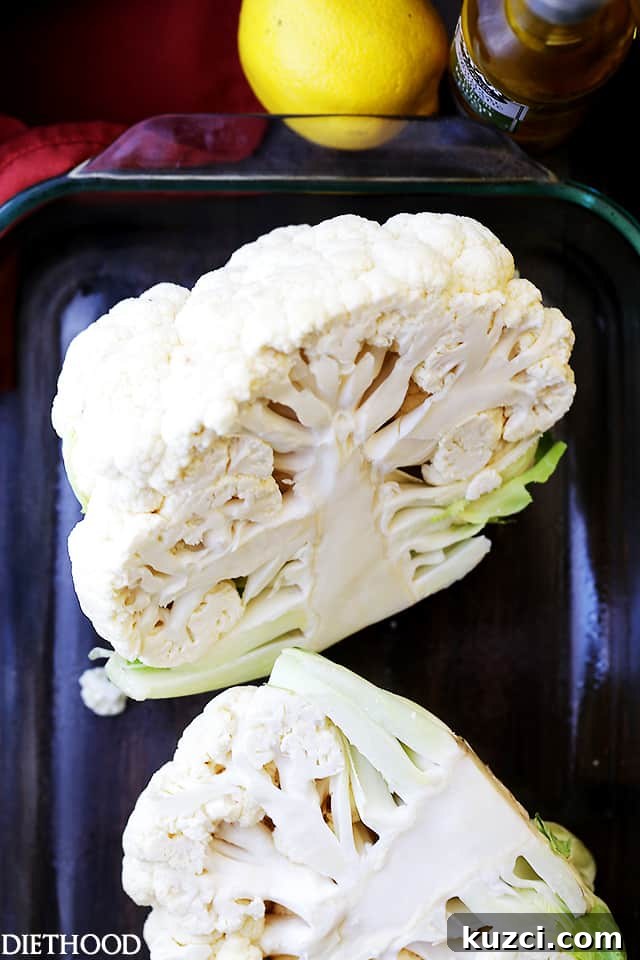Make crispy roasted cauliflower tossed in olive oil and seasoned with lemon zest, paprika, and thyme. An easy, flavorful vegetable side dish! A head of cauliflower cut in half on a baking sheet.