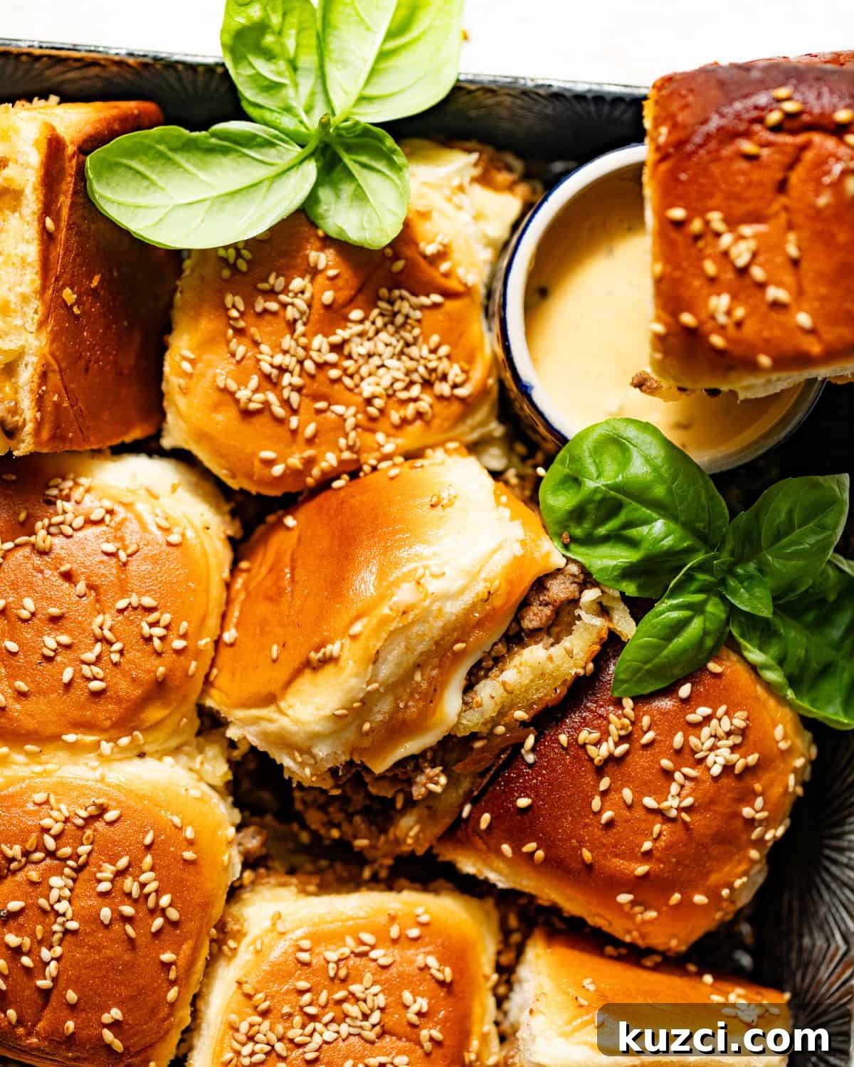 cheeseburger sliders with hawaiian rolls on a serving board with burger sauce and fresh basil.