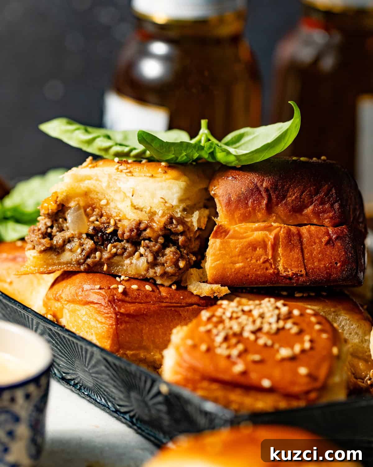 cheeseburger sliders on a baking sheet garnished with sesame seeds and basil.