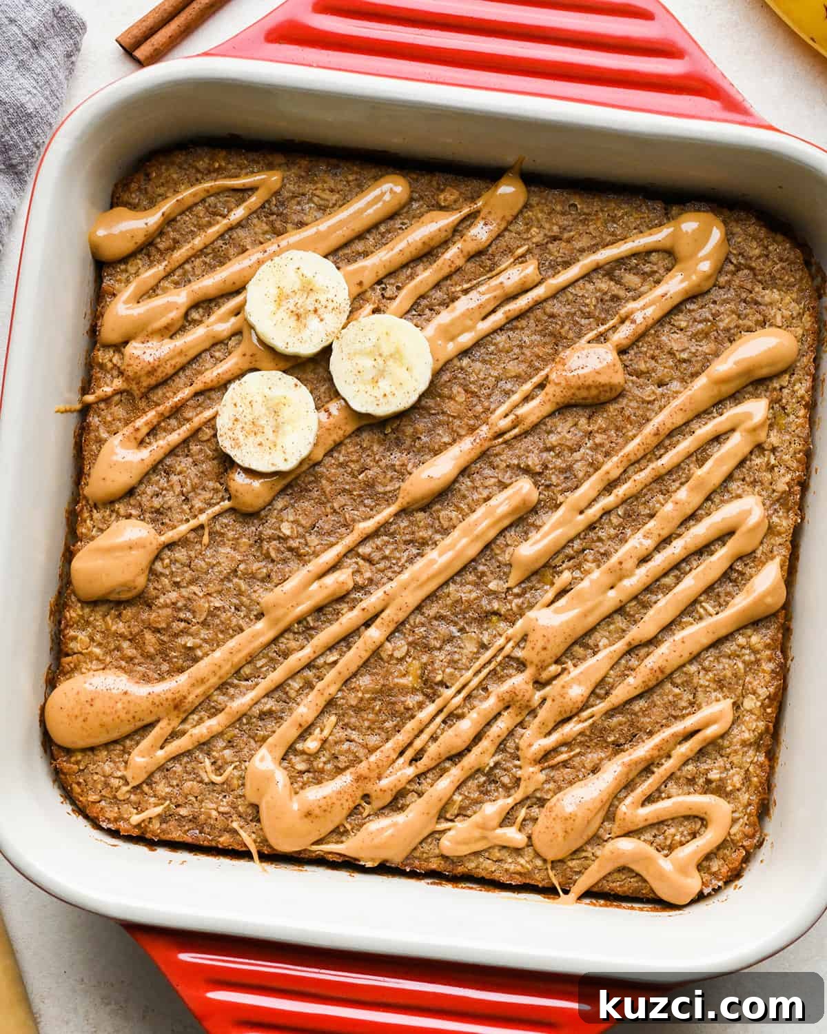 Peanut Butter Banana Baked Oatmeal Peanut Butter Banana Baked Oatmeal in a red square baking dish drizzled with peanut butter, topped with sliced bananas and cinnamon
