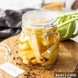 Jar of Pickled Kohlrabi, sitting on a round wooden board, with some herbs and spices around the edge.
