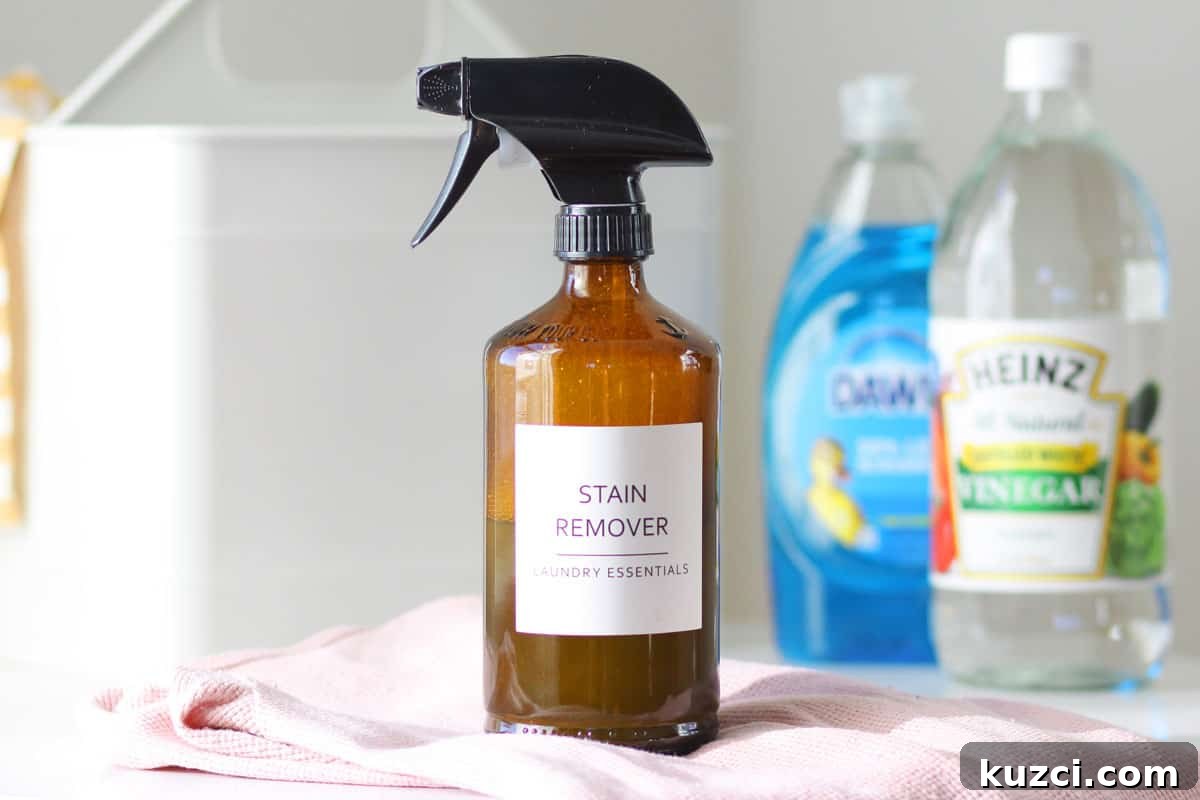 a glass amber spray bottle with a label that says 'stain remover laundry essentials' and a bottle of dawn dish soap and a bottle of distilled vinegar behind it