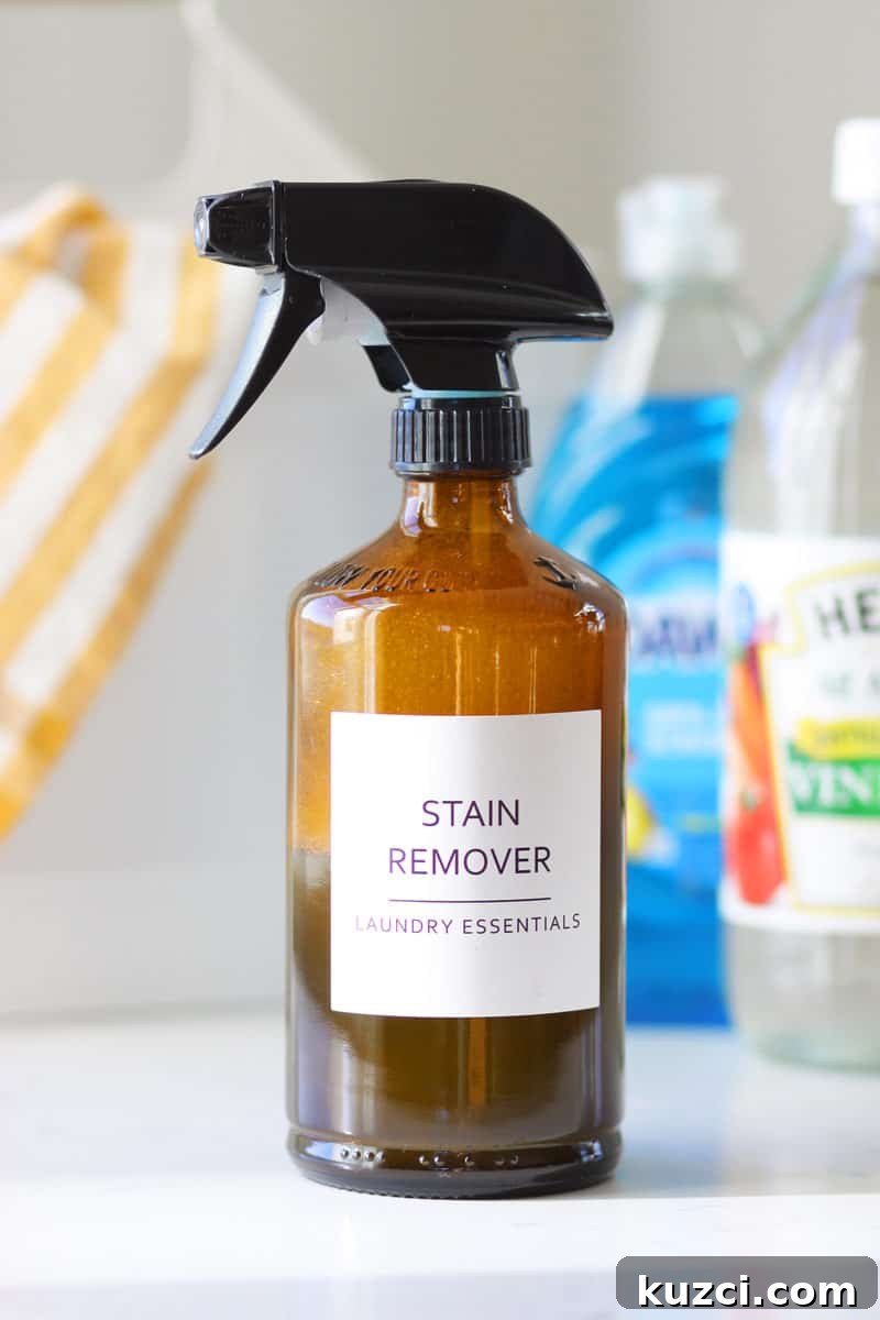 a glass amber spray bottle with a label that says 'stain remover laundry essentials' and a bottle of dawn dish soap and a bottle of distilled vinegar behind it