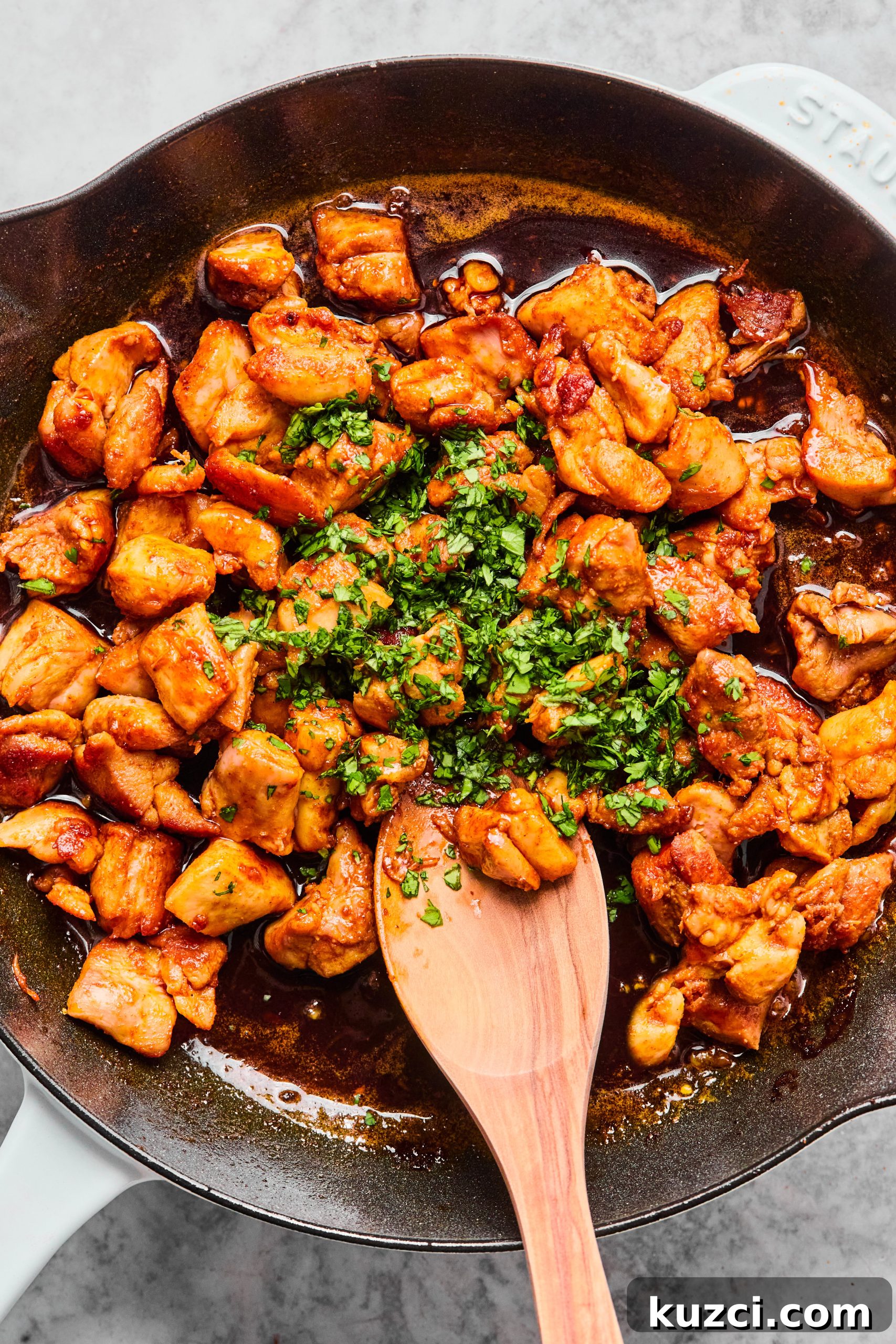 A large skillet filled with golden brown chicken bites tossed in a sweet orange honey sauce garnished with chopped cilantro