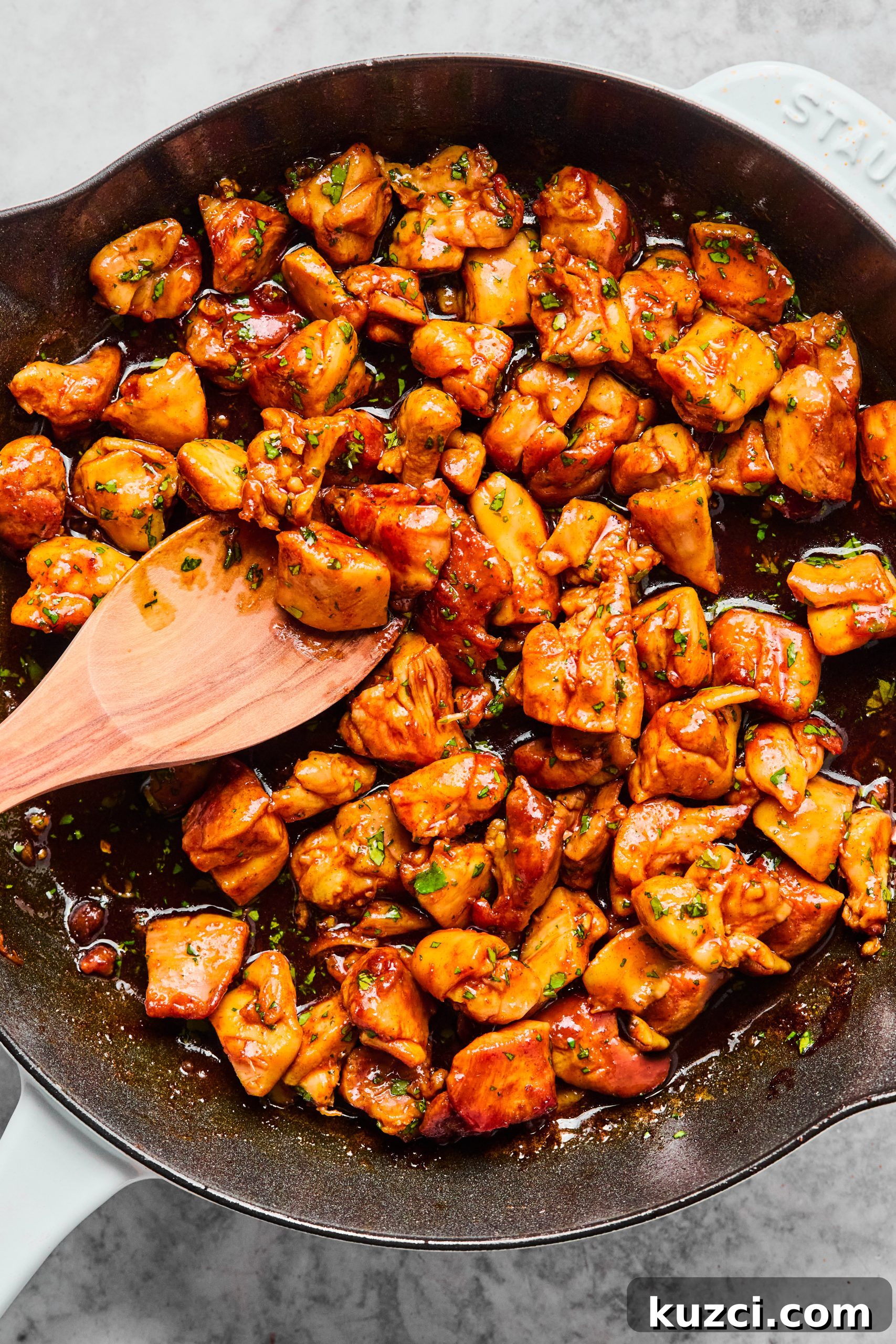 A large saute pan filled with freshly made cilantro orange chicken bites tossed in a sweet orange honey sauce