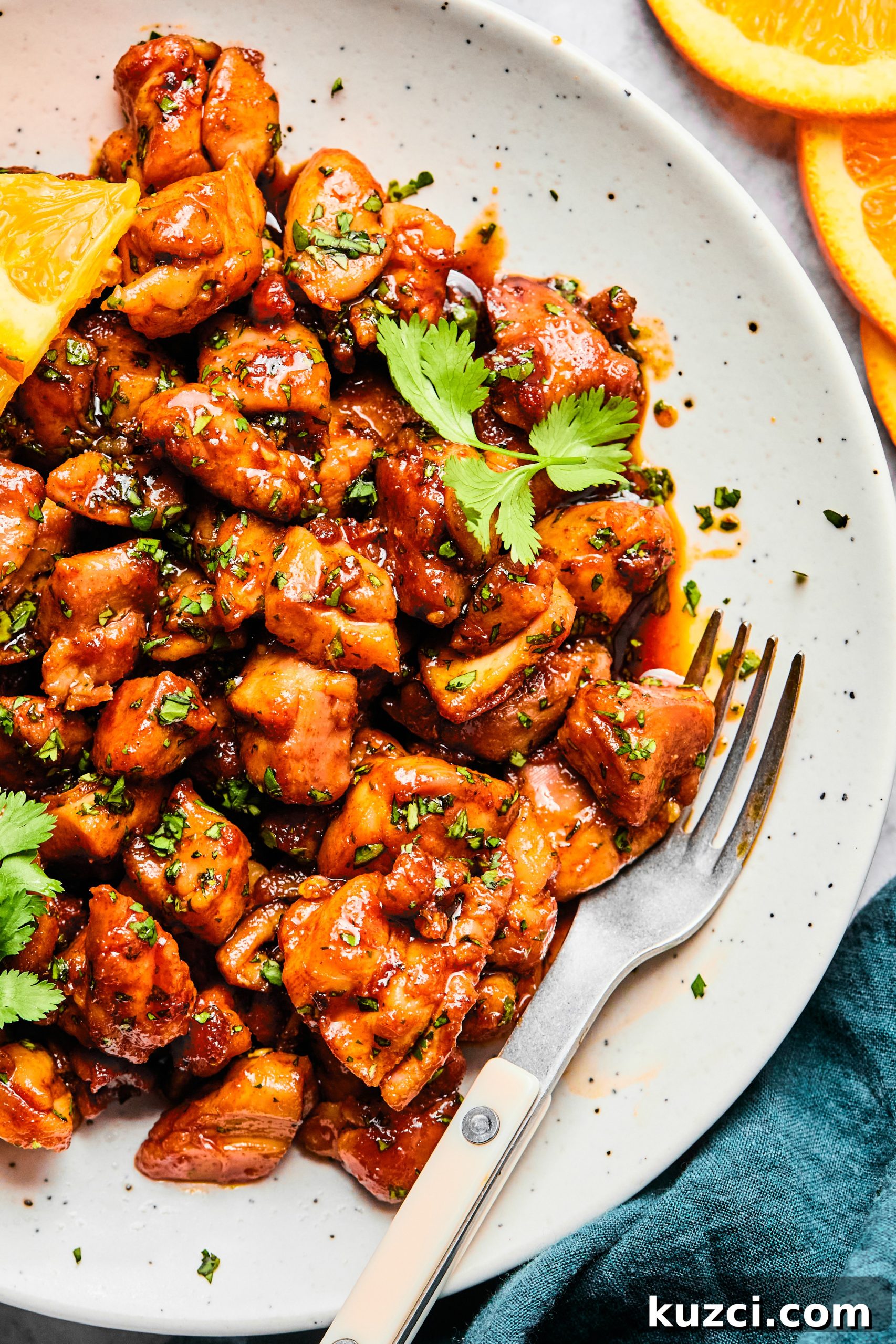 A close up photo of a small serving bowl filled with cilantro orange chicken bites sitting next to a fork