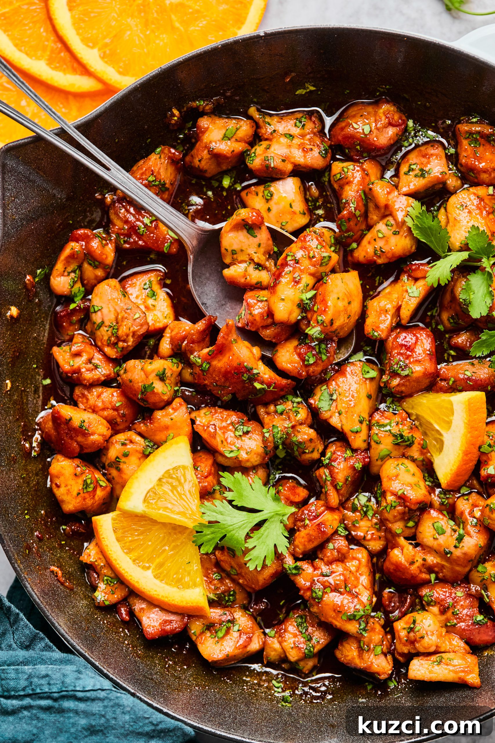 A large saute pan filled with cilantro orange chicken bites garnished with chopped cilantro and fresh orange slices.