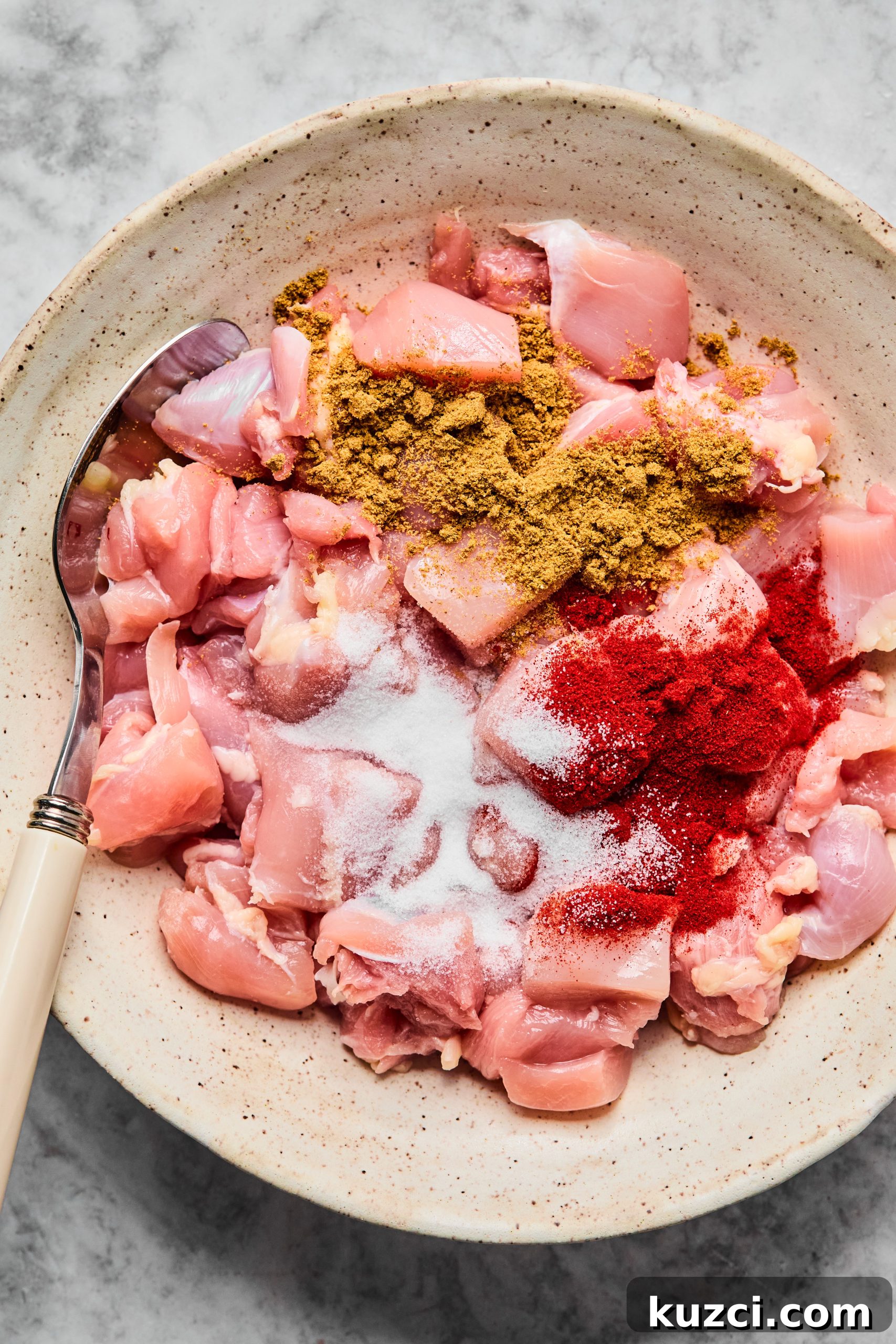 A white mixing bowl filled with diced chicken thighs, smoked paprika, cumin and salt.