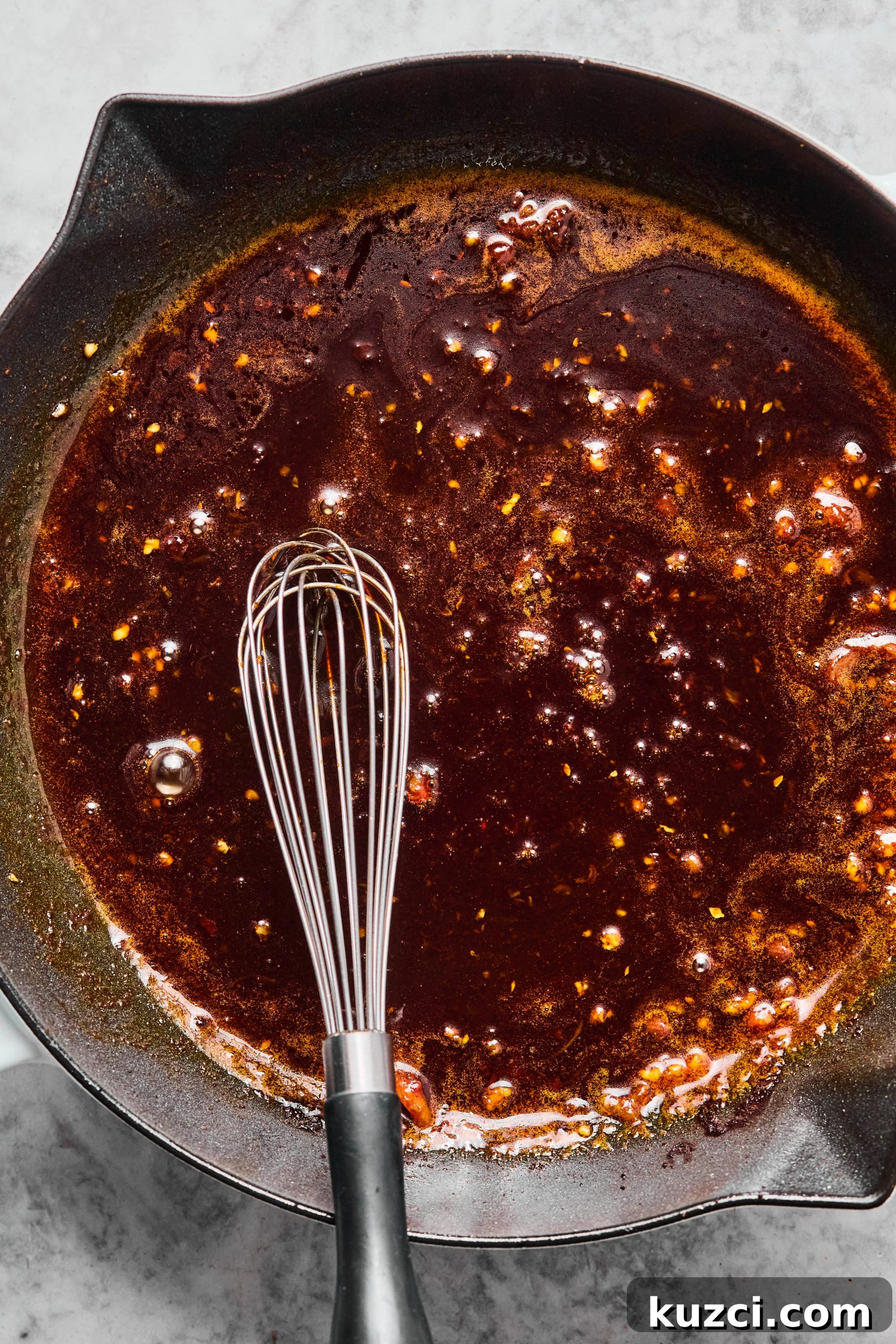 A large skillet filled with simmering orange honey sauce. (The sauce is reducing down until it becomes slightly thick.)