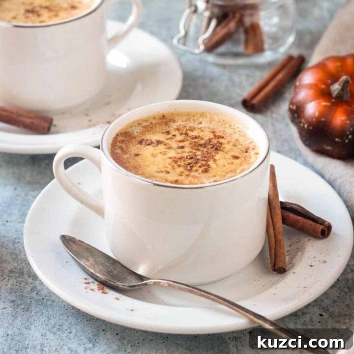 Cup of pumpkin spice coffee on a saucer with a spoon and two cinnamon sticks.