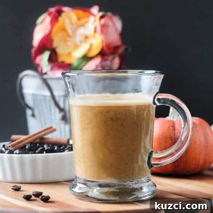 Front view of a glass of Pumpkin Latte. Orange decorative pumpkin and a small metal bucket of flowers in the background.