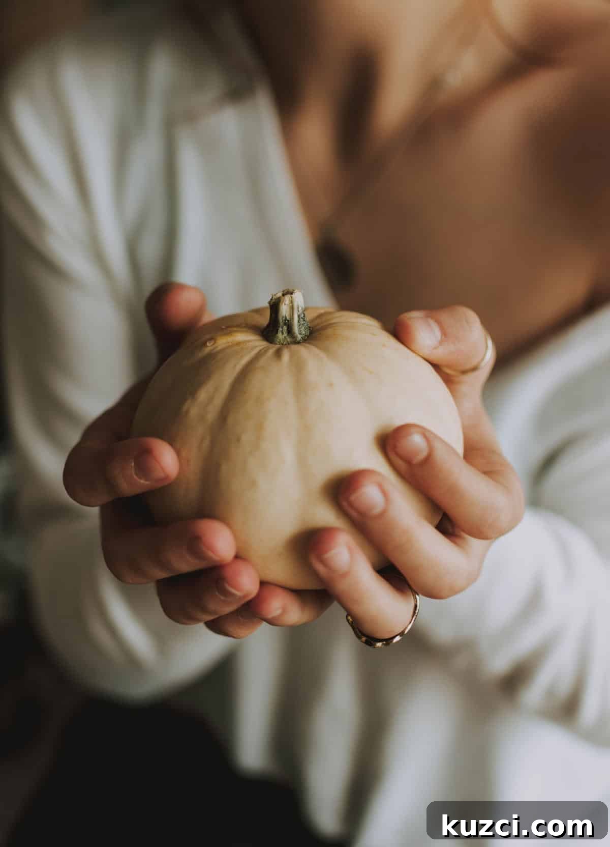 Woman in white sweater holding a small white pumpkin.