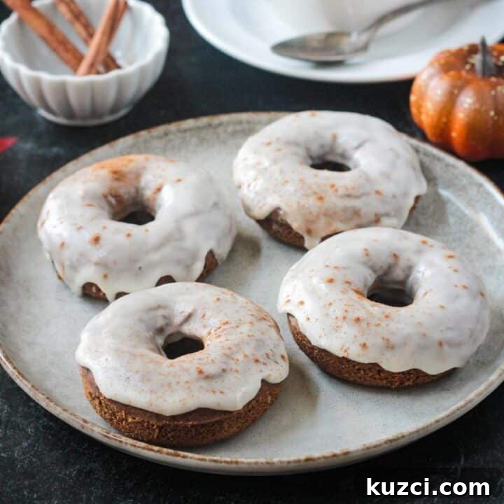Four iced pumpkin donuts on a plate.