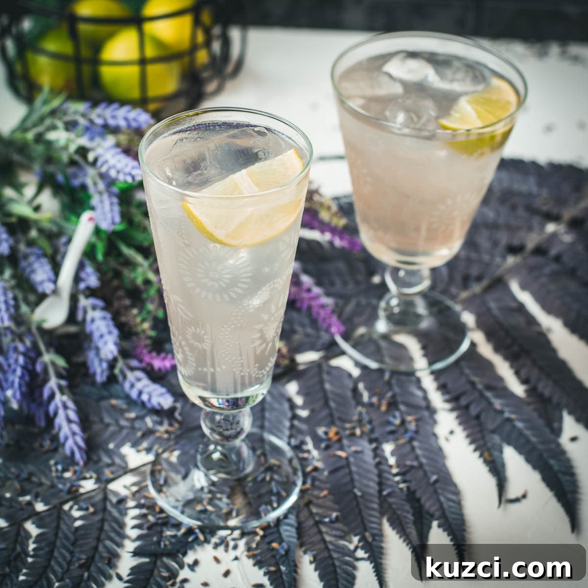 Two glasses of lavender Moscow Mule arranged on dark purple leaves.