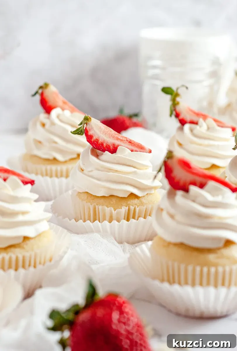 Gluten Free Dairy Free Strawberry Shortcake Cupcakes 2 Strawberry shortcake cupcakes all sitting on a table. They are each topped with a swirl of white whipped cream and a bright red strawberry slice is on top of each cupcake.