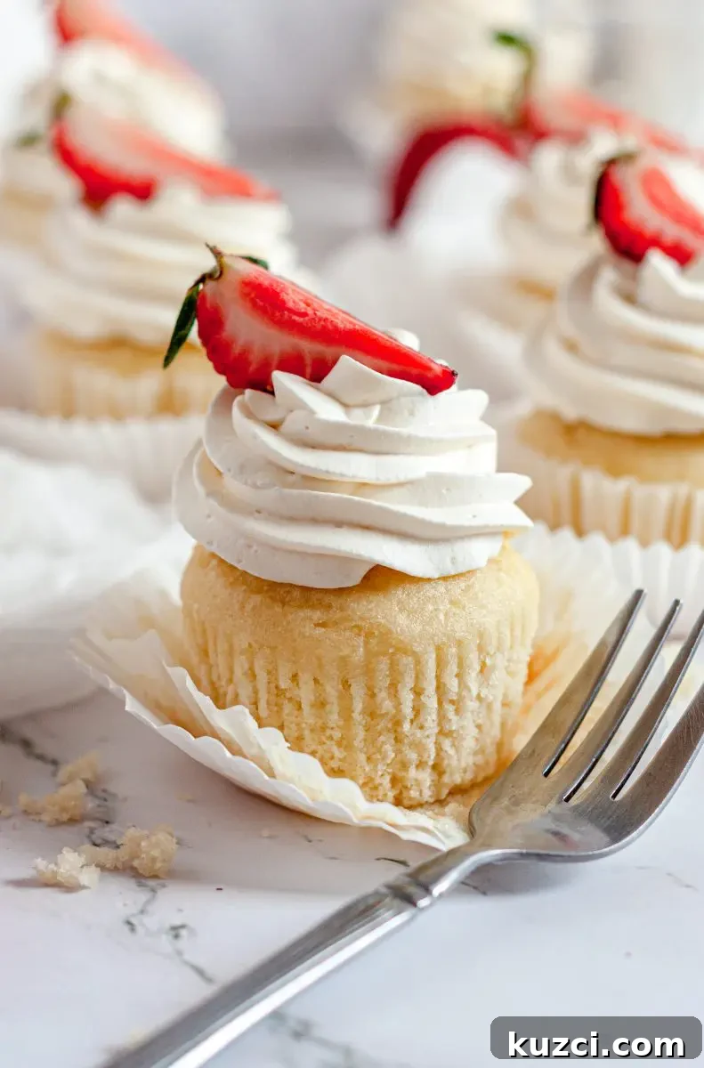 Gluten Free Dairy Free Strawberry Shortcake Cupcakes 3 A white strawberry shortcake cupcake topped with a swirl of whipped cream and a sliced strawberry is on the top. There is a fork sitting in front of the cupcake.