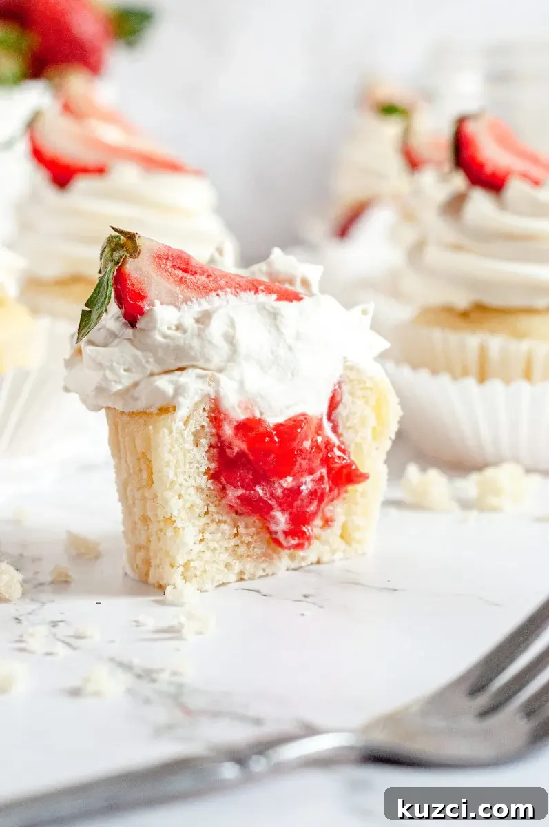 Gluten Free Dairy Free Strawberry Shortcake Cupcakes 4 A close up picture of a strawberry shortcake cupcake. It is topped with a swirl of white whipped cream with a bright red strawberry slice on top. It has been cut in half and you can see that is is filled with bright red strawberry filling.