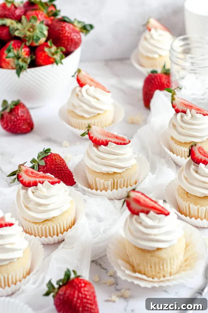 Gluten Free Dairy Free Strawberry Shortcake Cupcakes 5 Strawberry shortcake cupcakes all sitting on a table. They are each topped with a swirl of white whipped cream and a bright red strawberry slice is on top of each cupcake.