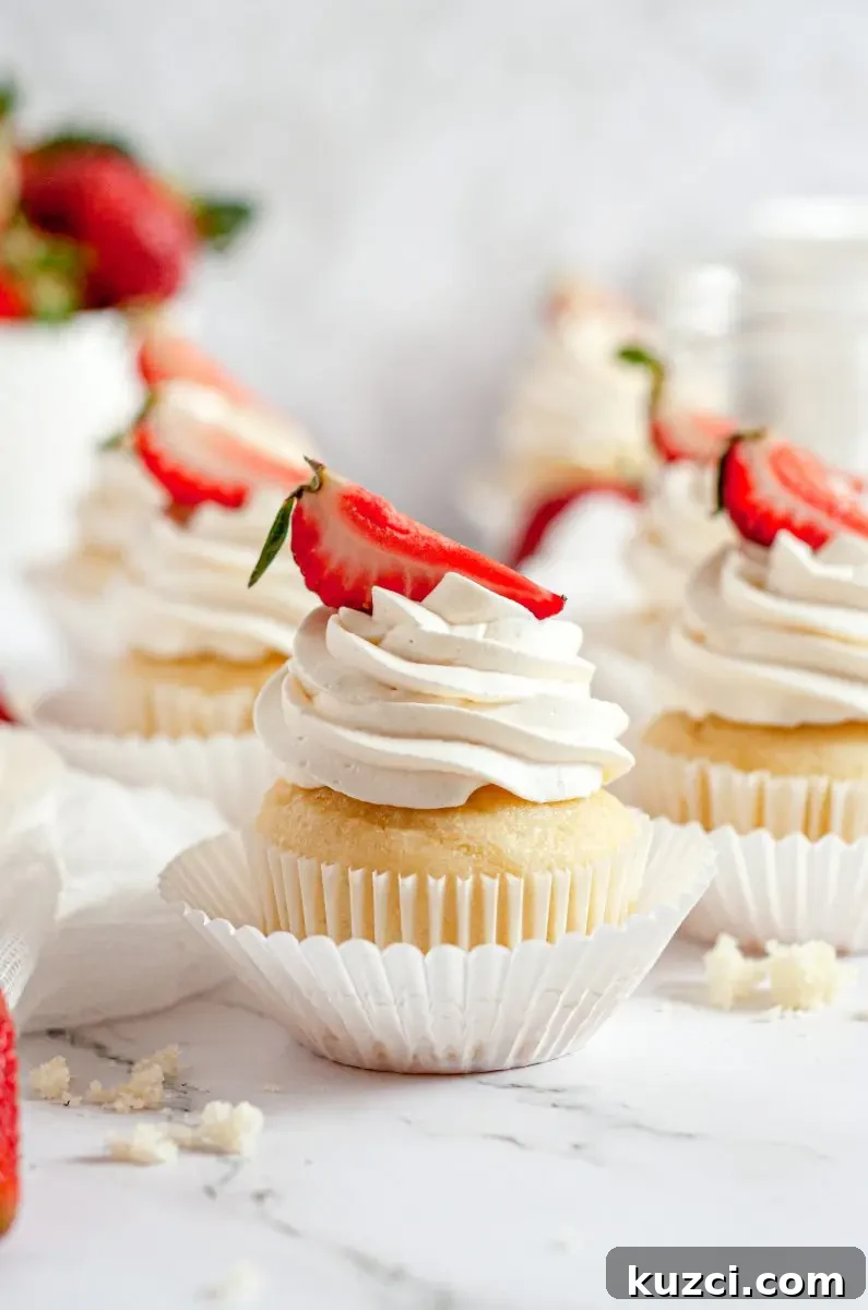 Gluten Free Dairy Free Strawberry Shortcake Cupcakes 6 A close up picture of a strawberry shortcake cupcake. It is topped with a swirl of white whipped cream with a bright red strawberry slice on top.