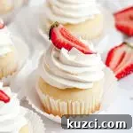 A strawberry shortcake cupcake topped with white whipped cream and a bright red sliced strawberry on top of the whipped cream.