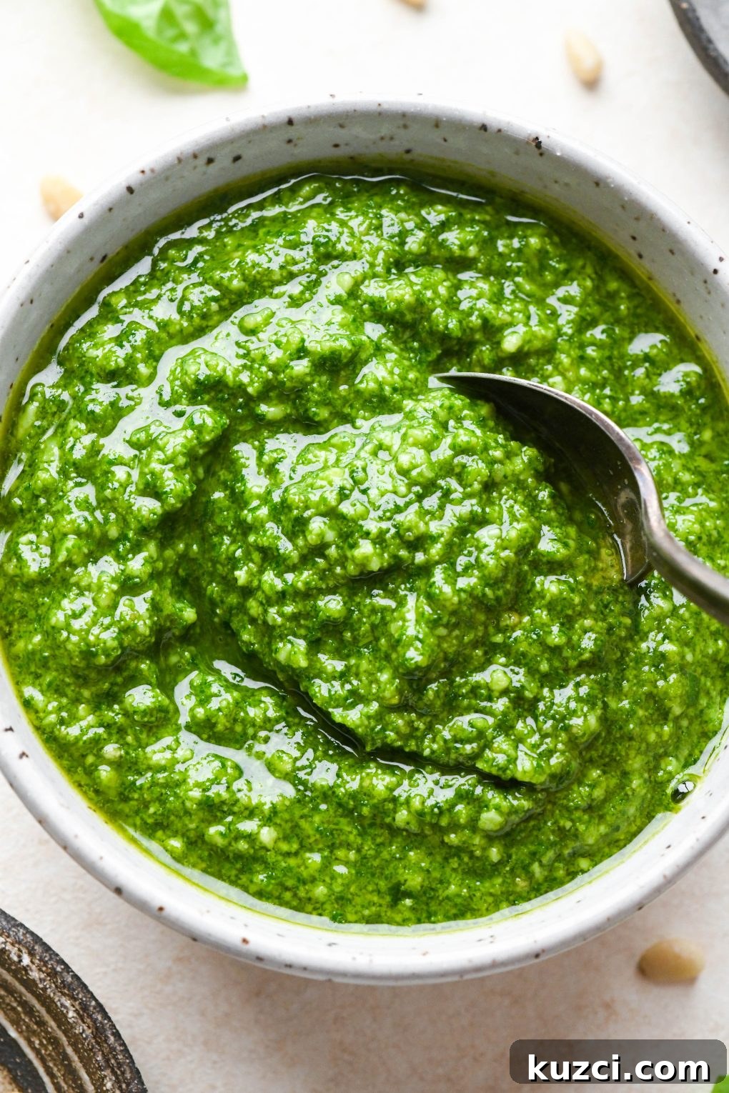 Homemade Basil Pesto - Vegan-Friendly Recipe 2 Homemade basil pesto in a small speckled bowl with a spoon dipping in.